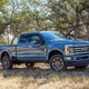 A very large blue 2023 Ford F-350 Super Duty is parked in a copse of trees.